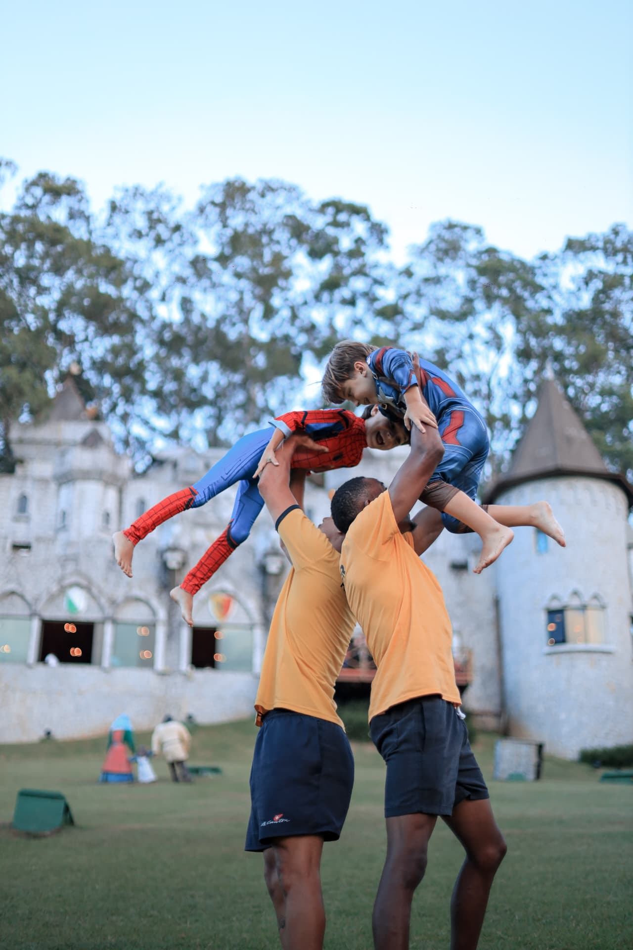 Pai brincando com filhos fantasiados de super-heróis em frente ao castelo